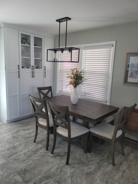 Charleston SC dining room makeover — rustic farmhouse trestle table with cross-back chairs, tall white glass-front china cabinet, black geometric cage pendant light, and fresh floral centerpiece designed by KDC Interiors