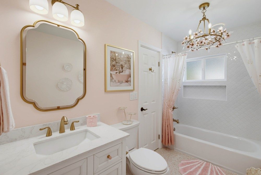 Girls' mermaid bath after renovation — gold scalloped mirror, whimsical floral chandelier, white scalloped shower tile, and a blush pink curtain, by KDC Interiors
