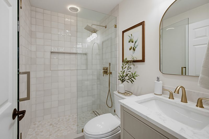 After: a white zellige tile shower, sage reeded-front vanity, arched mirror, and olive branch art, by KDC Interiors