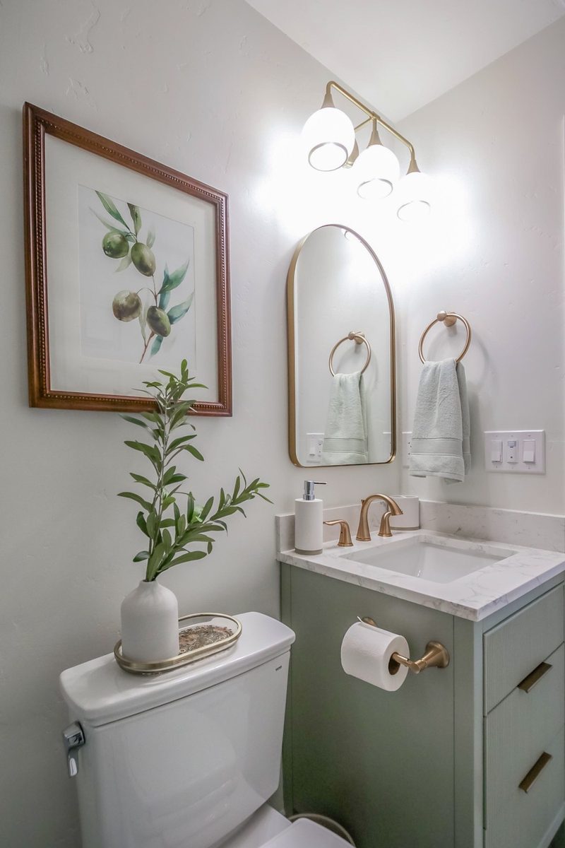 Sage reeded-front vanity with an arched mirror and olive branch art, by KDC Interiors