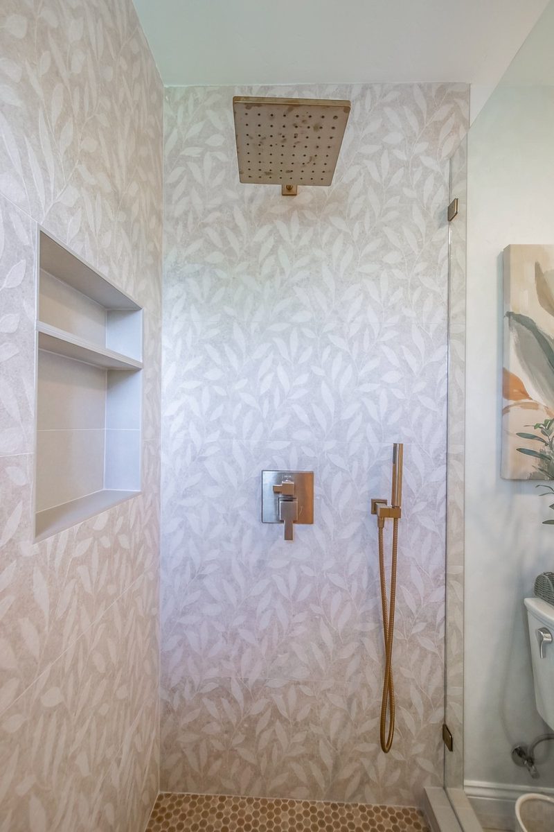 Shower with leaf-pattern tile and brass fixtures, by KDC Interiors
