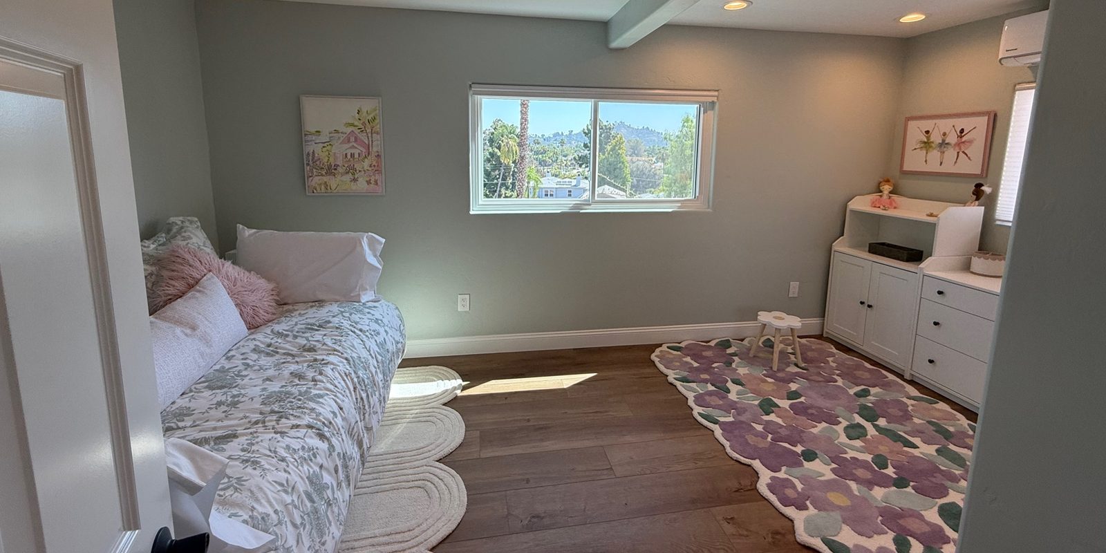 After: the guest suite with a daybed, floral rug, and white dresser at the same window, by KDC Interiors