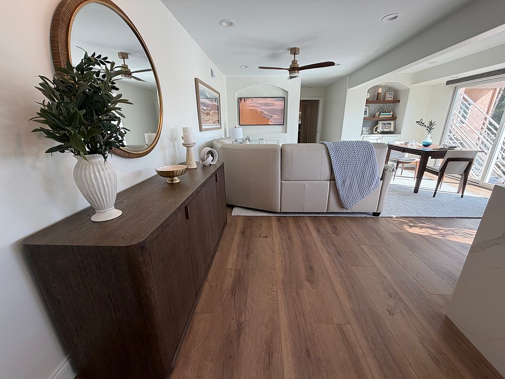 Open lower-level living area after renovation — wood sideboard with a round mirror, leather sectional, and windows onto the deck, by KDC Interiors