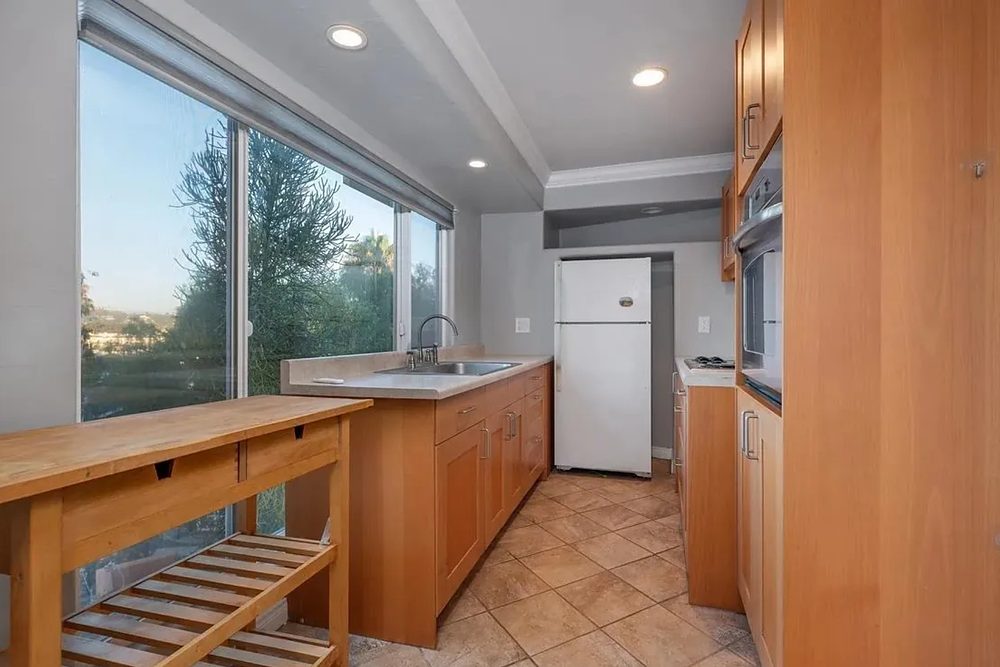 Before: the enclosed kitchenette with a wood peninsula, white refrigerator, and dated tile floor