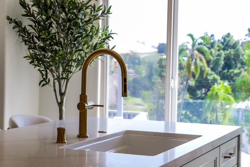 Brass faucet and sink framed by the window and the outdoor view, by KDC Interiors