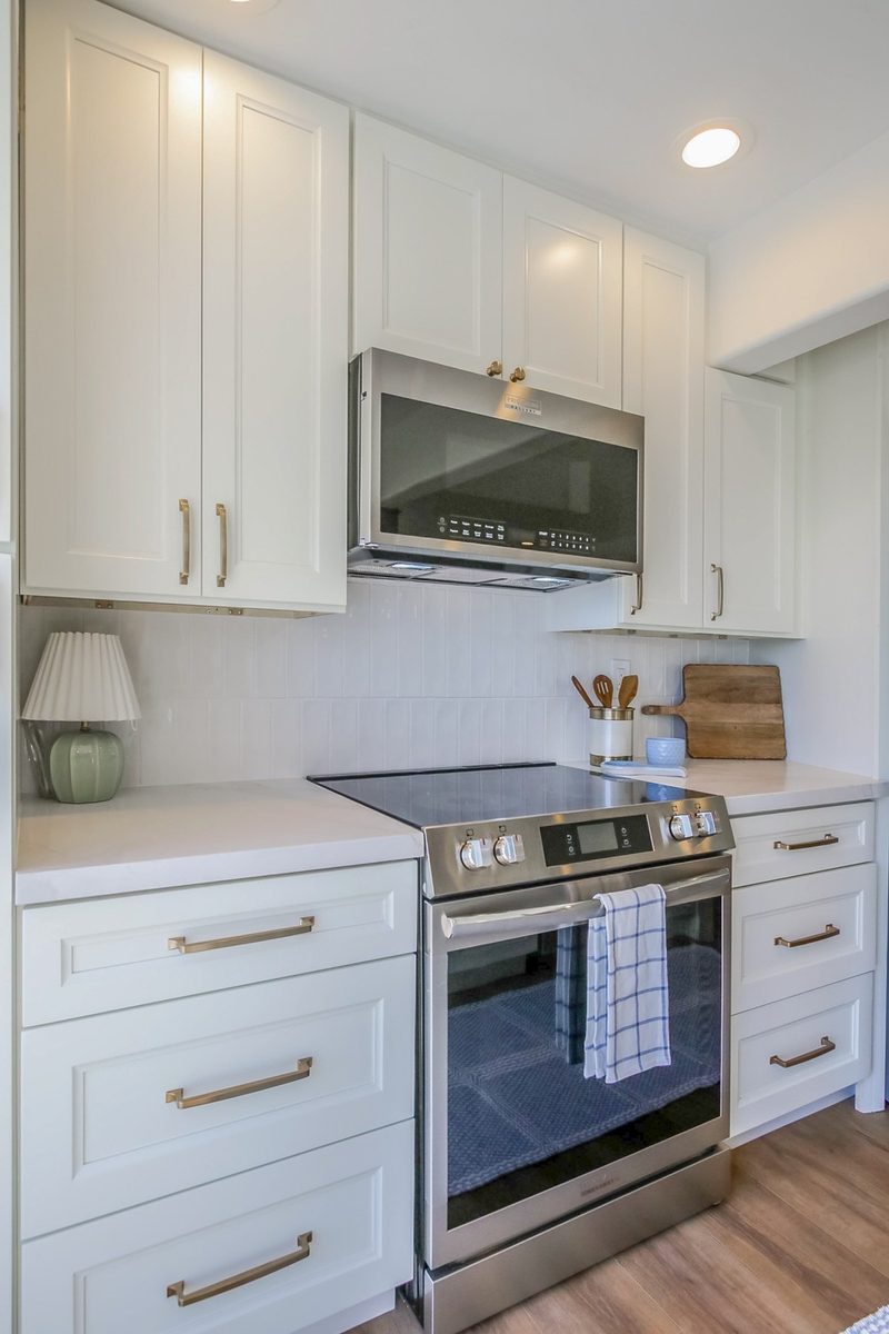 Range wall with white shaker cabinetry and a built-in microwave, by KDC Interiors