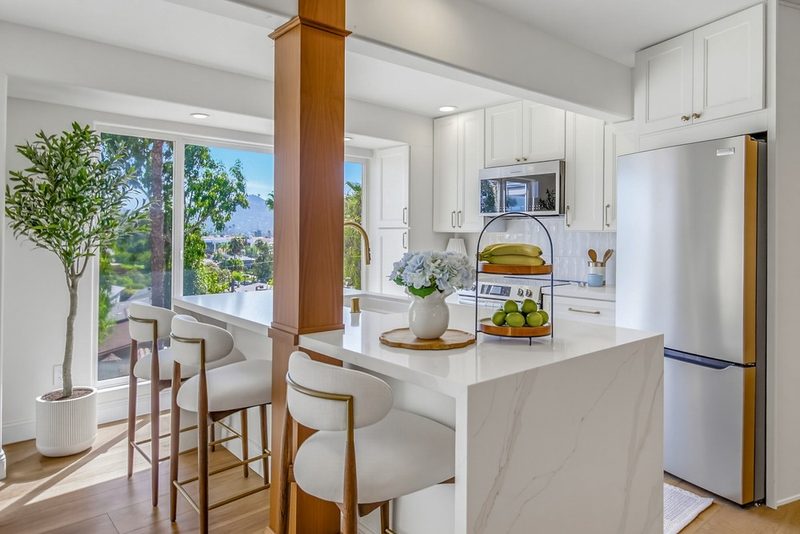 Waterfall quartz island with counter stools, brass hardware, and a window view, by KDC Interiors
