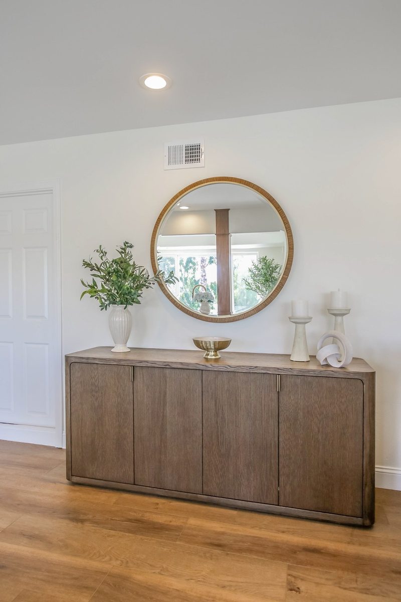 Wood sideboard with a round mirror and layered accessories, by KDC Interiors