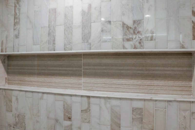 Shower niche in striated stone framed by marble tile, by KDC Interiors