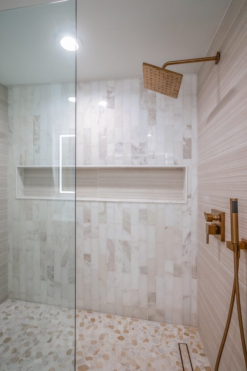 Shower with a lit niche and a pebble tile floor, by KDC Interiors