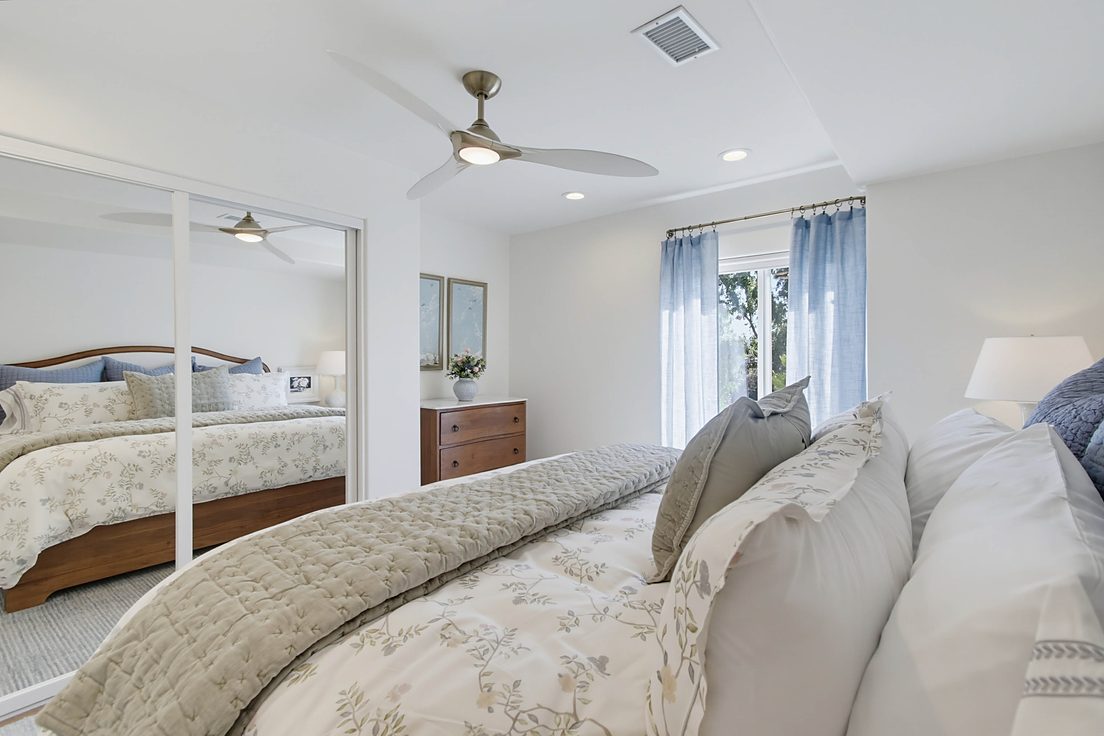 After: the primary bedroom with a king bed, mirrored closet doors, and blue light-filtering curtains, by KDC Interiors