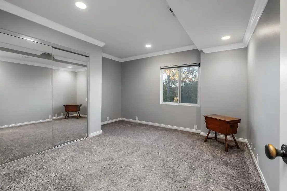 Before: the empty primary bedroom with gray carpet and mirrored closet doors