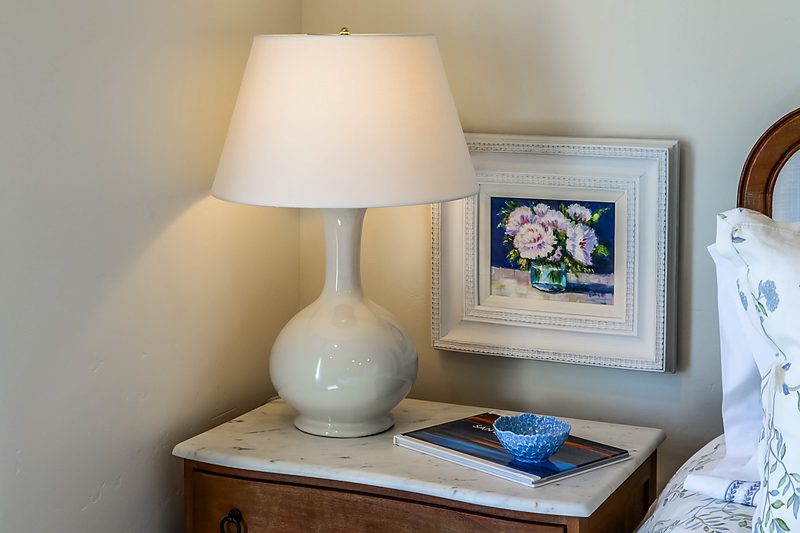 Nightstand with a ceramic lamp and floral artwork, by KDC Interiors